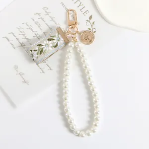 Detail of pearl keychain with floral embroidery and golden vintage coin charm