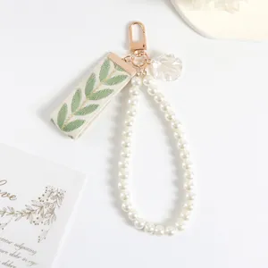 Detail of beaded pearl keychain featuring golden leaf ribbon and a shell pendant