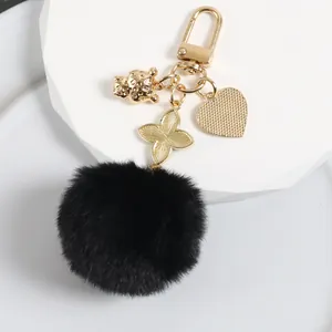 Detailed close-up of fluffy black pompom keychain with golden clover and heart charms