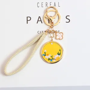 Close-up of yellow floral daisy embroidery keychain with gold metal buckle and pendant