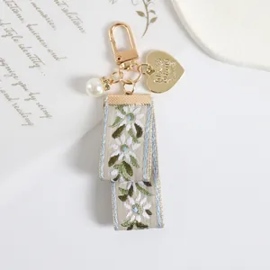 Macro detail of embroidered floral ribbon keychain with golden heart charm and pearl