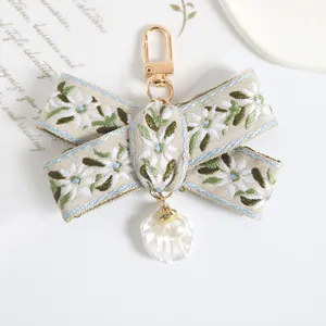Detail of embroidered floral bow keychain with pearl and shell pendants and gold clasp