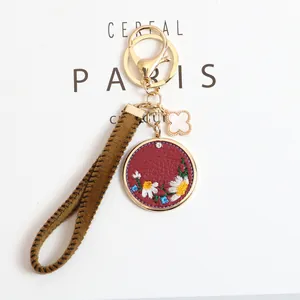 Detailed view of red leather keychain with daisy embroidery and clover charm