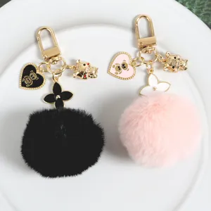 Plush bear keychain with faux fur pompom and golden heart charm on white background