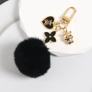 Close-up of black pom-pom keychain with gold bear heart and zodiac tiger charms