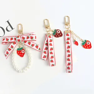 Detailed view of three strawberry-themed keychains with pearls and red ribbon charms
