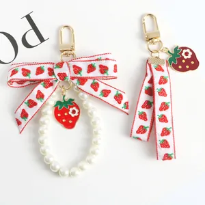 Detail of strawberry charm keychain with pearl loop and printed ribbon on white background