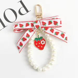 Detail of strawberry charm keychain with white pearl loop and embroidered ribbon bow