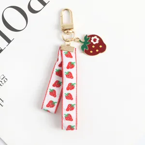 Detail of strawberry keychain with gold clasp, red enamel pendant, and printed ribbon