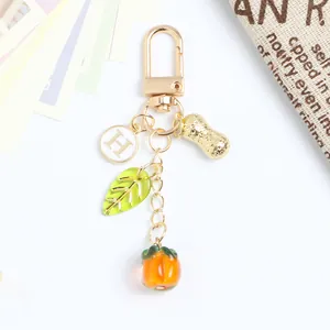 Detail of keychain with persimmon, peanut, leaf, and letter H charms on white background