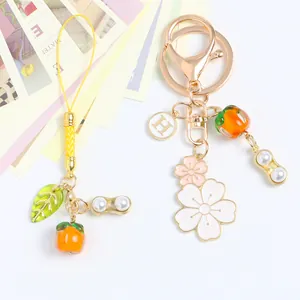 Close-up of golden keychain with persimmon, flower and peanut pendants on yellow cord