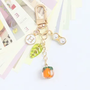 Detail of golden keychain with persimmon, peanut charm, and pearl on white cards