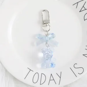 Close-up of a light blue crystal bear keychain with a bow on a white plush background
