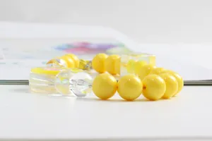 Detail of yellow acrylic beaded phone strap with pink heart charm on white surface