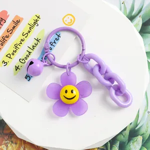 Détail du porte-clés fleur sourire en acrylique violet avec chaîne mate et clochette sur pierre