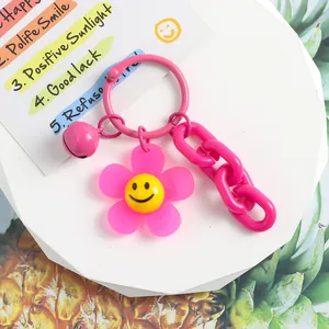 Détail d'un porte-clés fleur rose en acrylique avec smiley jaune et petite clochette
