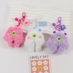 Detailed view of plush monster keychains in pink, white, and purple with colorful charms