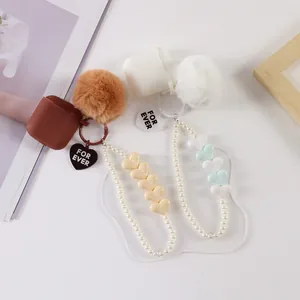 Detail showing silicone AirPods cases with plush pompons and faux pearl heart charms