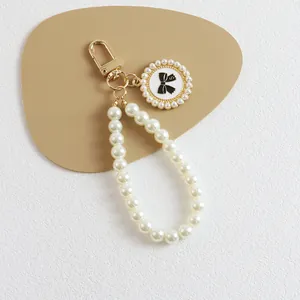 Detail of pearl keychain with gold clasp and number 5 bow charm on leather surface