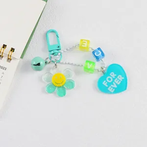 Détail d'un porte-clés fleur en acrylique avec clip vert menthe, cœur bleu et perles lettres
