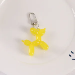 Detailed view of glossy yellow resin balloon dog charm with silver lobster clasp on white plate
