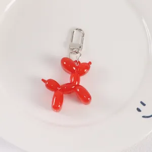 Close-up of bright red jelly balloon dog keychain with silver metal clasp on white tray