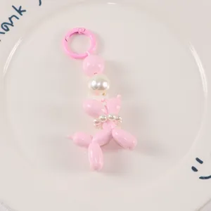 Detail of pink balloon dog keychain with white pearl collar on decorative white plate