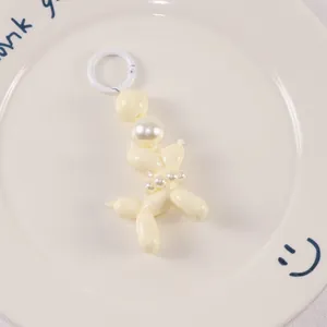 Detail of a cream resin balloon dog keychain with pearl beads on a white ceramic plate