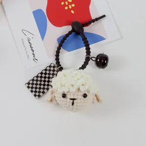 Handmade crochet sheep hair tie with black bell and checkered tag on gray background