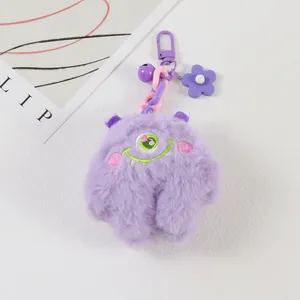 Detail of purple plush monster keychain with embroidered eye, bell and flower charm