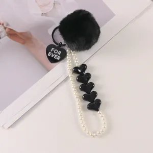 Detail of black faux fur pompom keychain with white pearl beads and heart charms