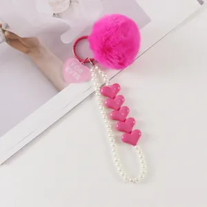 Detail view of pink fluffy faux fur pompom keychain with heart charm and pearl wristlet