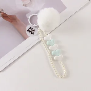 Detail of plush fur ball keychain with imitation pearls and heart charms on white background