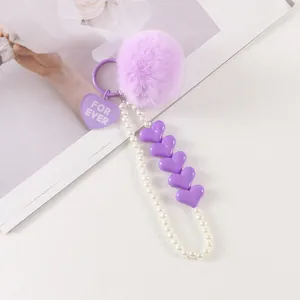 Detail of purple fluffy fur pompom with white pearls and heart charms keychain