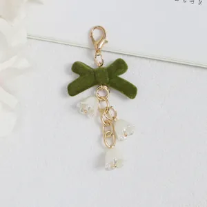 Detalle de llavero con lazo de terciopelo verde oscuro y flores blancas de lirio de valle