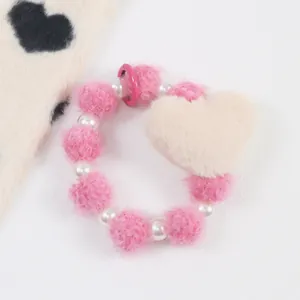 Gros plan d'un bracelet peluche rose en forme de cœur avec perles et pompons doux