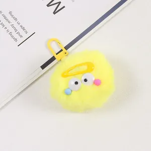 Gros plan sur un porte-clés pompon jaune en peluche avec yeux et accents colorés