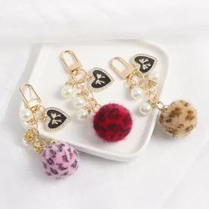 Porte-clés cœur en peluche léopard avec perles et fermoir doré sur plateau blanc