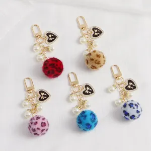 Détail de porte-clés pompon léopard avec perles blanches et breloques en forme de cœur