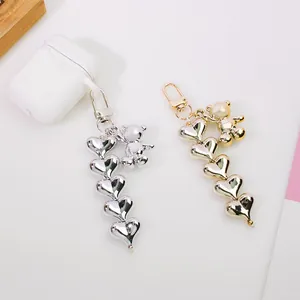Silver metallic heart pendant with bear charm on a white wireless earphone case
