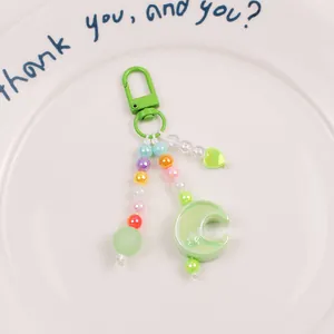 Close-up of pastel beaded keychain with green crescent moon and heart pendant on white plate