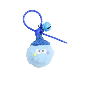 Blue fuzzy pompom keychain with mini knit hat, big eyes, and bell on white background