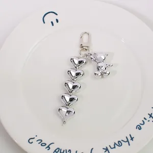 Close-up of silver bear keychain with five heart charms on a white ceramic plate