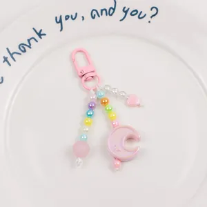 Detail of pink beaded moon keychain with star charms and acrylic heart on a white plate