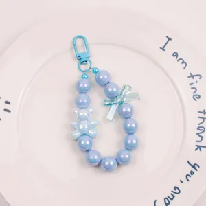 Detail of light blue bead keychain with a matte bear charm and iridescent bow on a plate