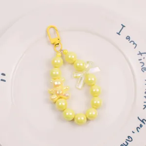 Detail of yellow beaded keychain with 3D cartoon bear and iridescent charms on white plate
