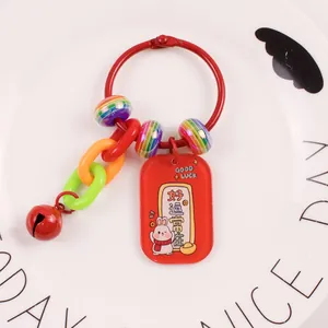 Detail of red rabbit keychain with good luck charms and metallic bell on white plate