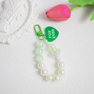 Dettaglio di ciondolo in perle con cuore verde e testo inciso For Ever inciso