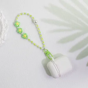 Detail of beaded floral keychain with green pearls on a white wireless earphone case