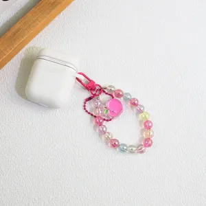 White silicone AirPods case with pink beaded peach keychain on white background